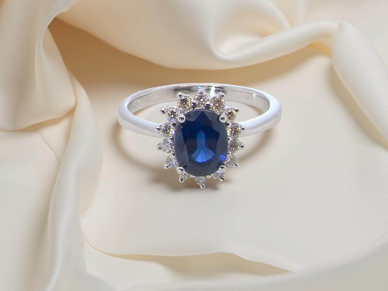 cluster ring featuring a striking mid–dark blue oval-cut sapphire at its centre, measuring approximately 8 × 6 mm 