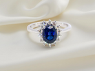 cluster ring with a striking mid–dark blue oval-cut sapphire at its centre, measuring approximately 8 × 6 mm (estimated 1.25 ct).
