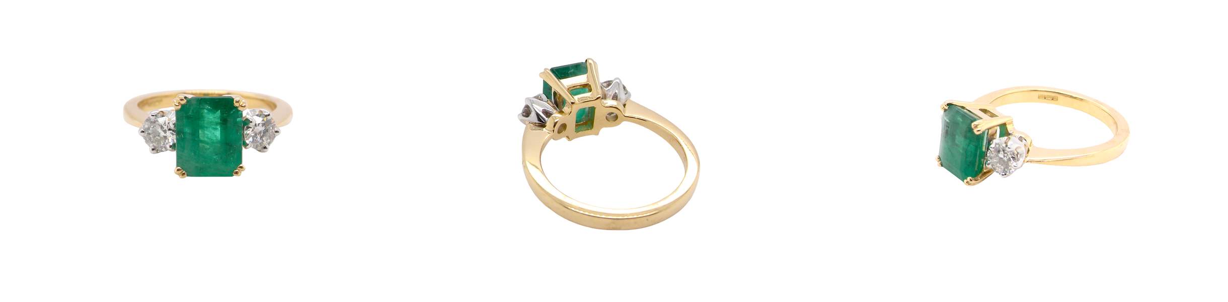 An exceptional three-stone ring featuring a vibrant step-cut emerald to the centre, measuring 8.6 x 7.0mm and weighing approximately 2.10 carats. The emerald displays a beautiful grass-green colour and is secured in a classic four-claw setting.