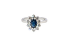  fine 18 carat white gold cluster ring. Features an oval cut dark blue sapphire centre stone 