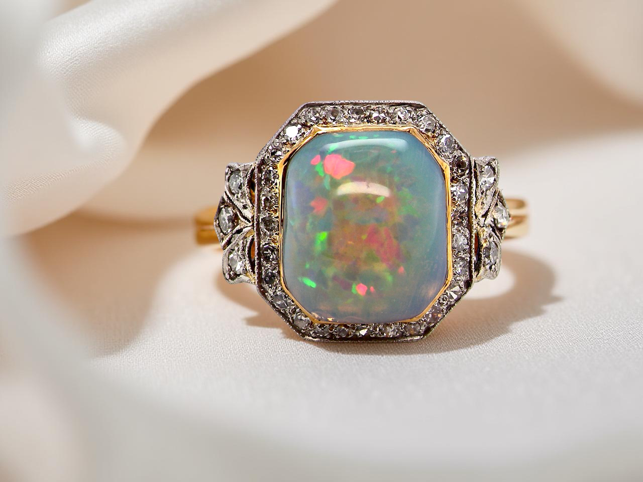 fine cabouchon cut opal shown is cushion shaped, measures 15x13 (5.78 carats) displaying a mass of vibrant colours, from flashes of fireglow orange, luminous greens, and lavender purples.
