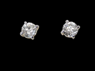 A pair of classic solitaire stud earrings featuring round brilliant-cut diamonds in four-prong silver settings, presented on a solid black background.