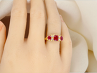 Gold ring with red gemstones on a person's finger against a soft white background