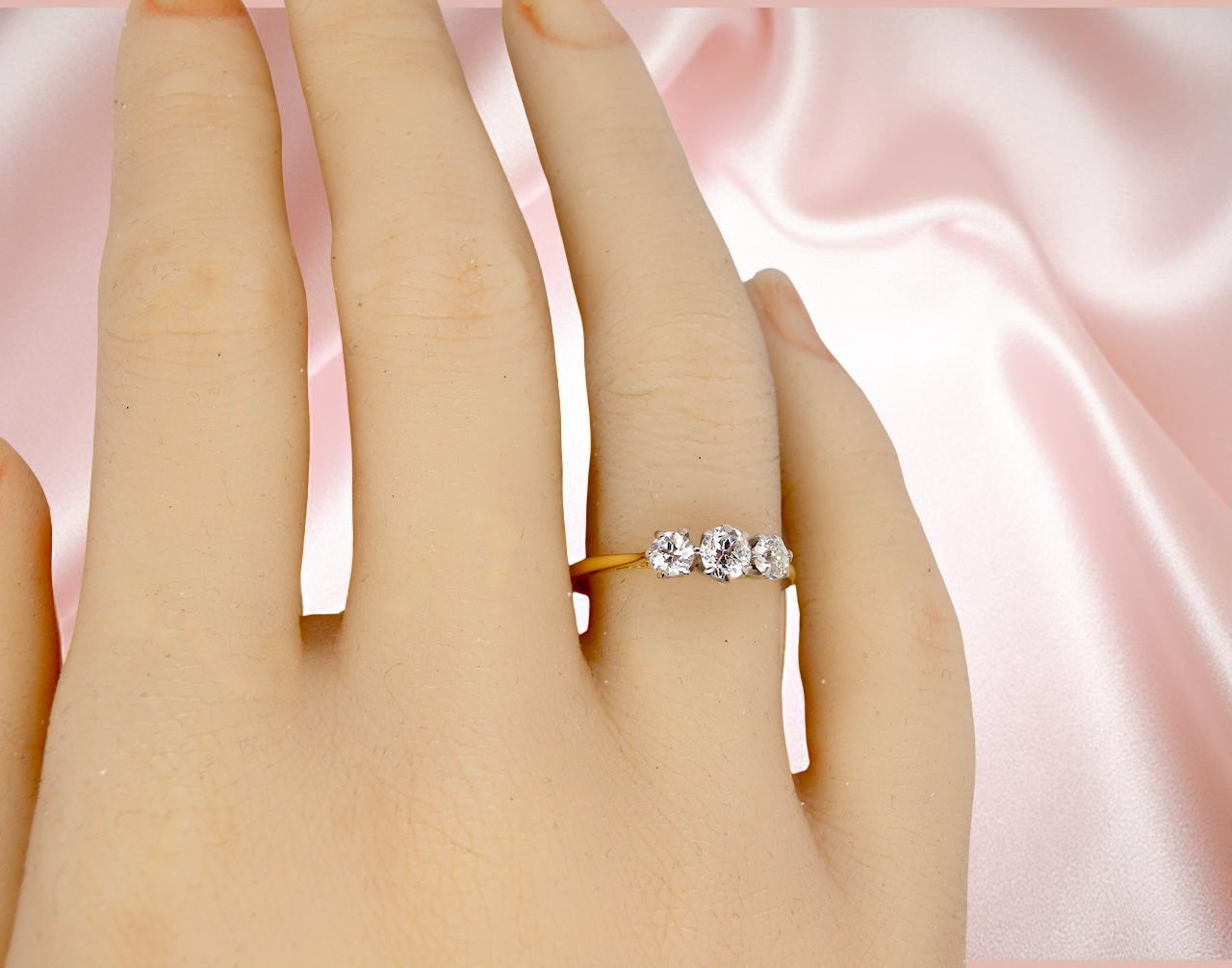 Silver ring with three diamonds on a finger against a pink satin background