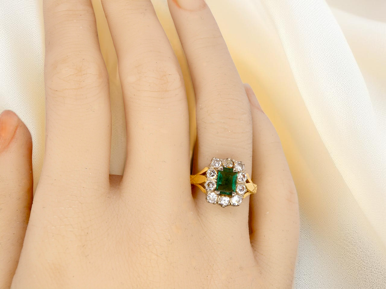 hand A cluster ring that features a rectangular emerald centre stone, 7x5mm . Deep green colour, natural inclusions that can be seen under an eye glass, but not easily visible via the naked eye.