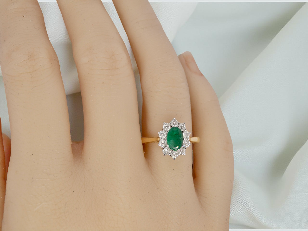 hand A fine traditional emerald and diamond cluster ring, featuring a vibrant oval-cut emerald to the centre measuring approximately 7 × 5 mm 