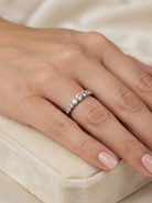 A close-up of a hand wearing a  eternity ring set with clear round-cut gemstones, resting on a soft cream velvet jewelry box.