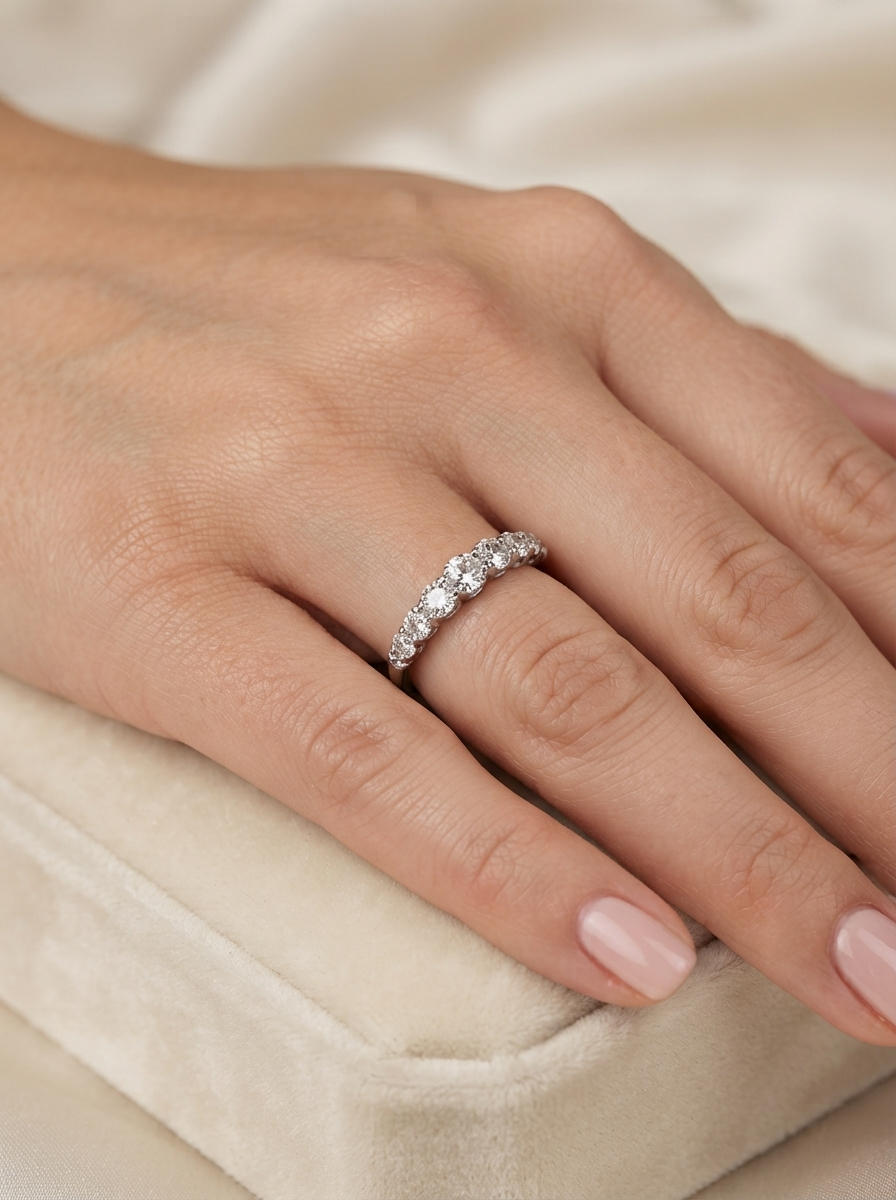 A close-up of a hand wearing a  eternity ring set with clear round-cut gemstones, resting on a soft cream velvet jewelry box.