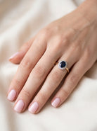 hand A pretty cluster ring that features an inky black blue sapphire that measures 8x6mm. Complimented by an outer border of  diamonds 