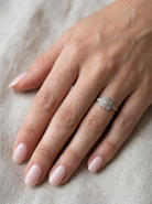 hand A pretty diamond cluster ring from the early part of the 20th century. A square head that has within it small white diamonds, measures 8x8mm, fancy shoulders also set with tiny diamonds.