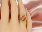 Rose gold ring on a person's finger against a soft pink background