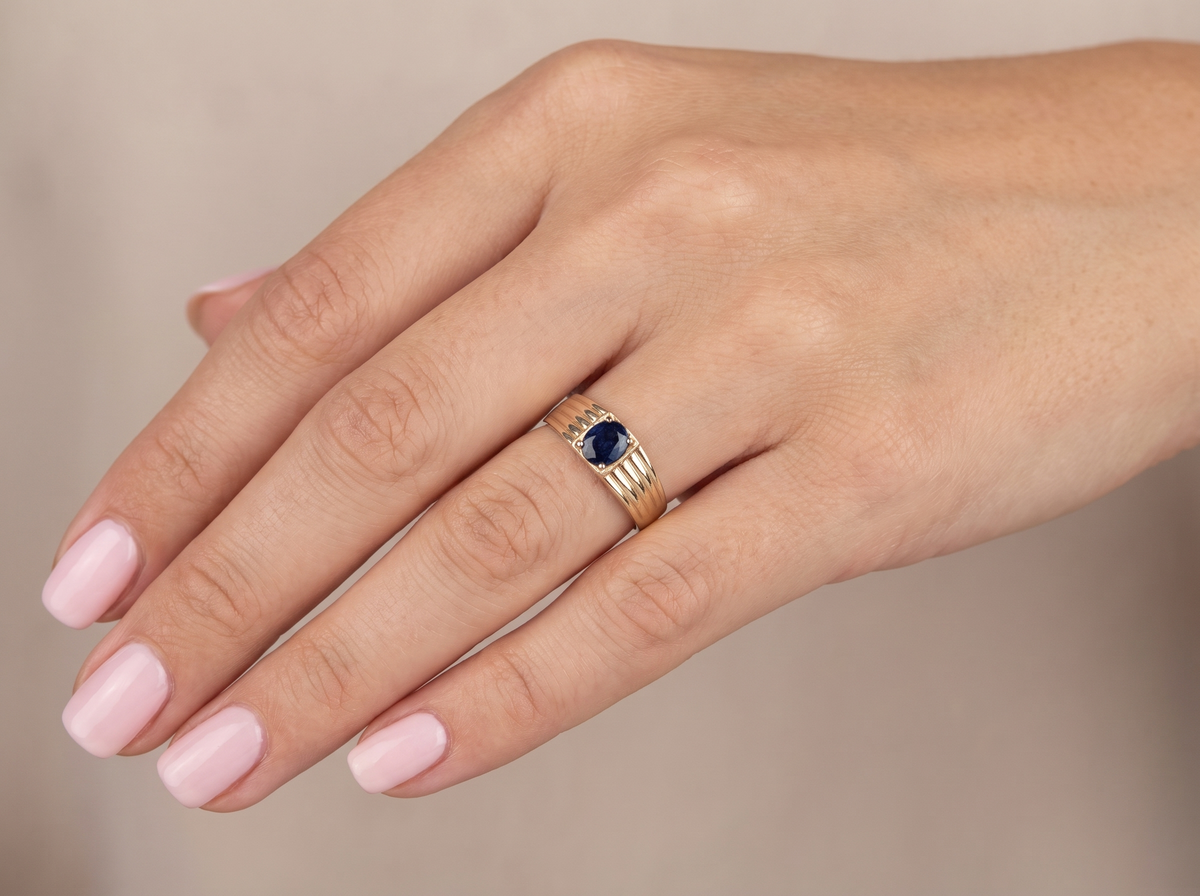 hand A solitaire dress ring that features an oval cut dark blue sapphire, 6x5mm. Wide ribbed patterned shoulders, 7mm width and tapering to a 3.8mm shank at the reverse.
