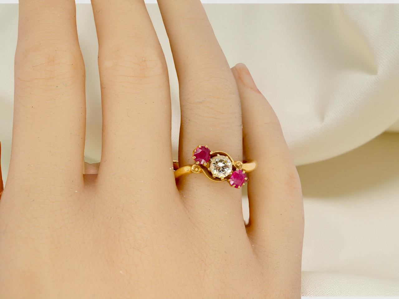 Gold ring with red gemstones on a person's finger against a neutral background