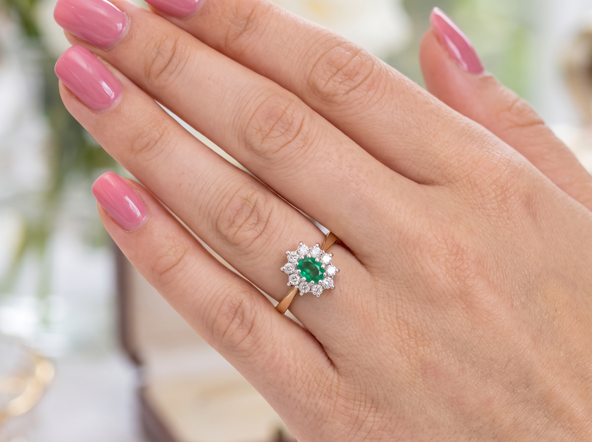 hand A traditional cluster ring. Features to the centre an oval shaped emerald, 5.5x4.5mm (est 0.35 carats) deep green colour.&nbsp;