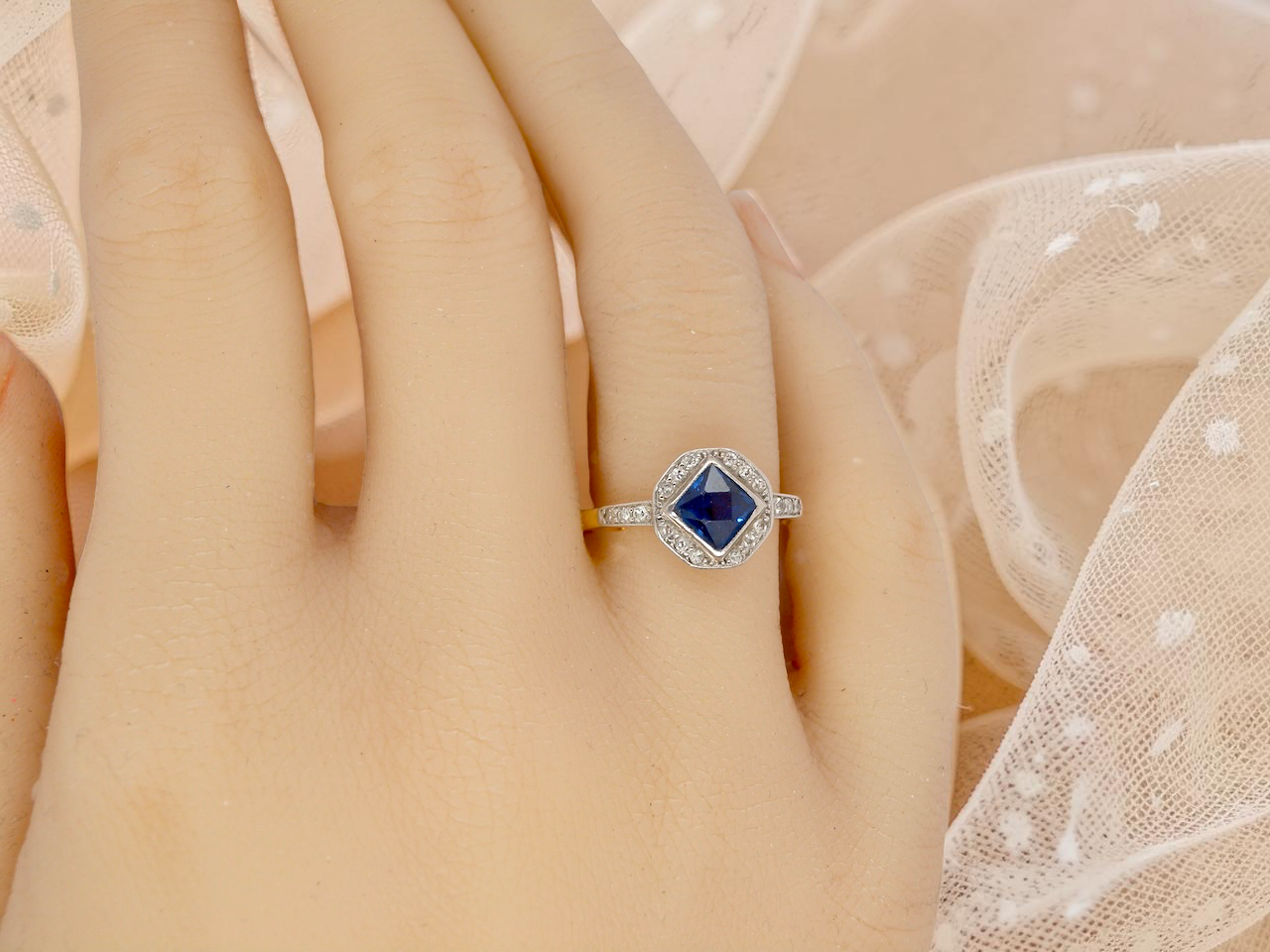 hand A very pretty Art Deco cluster ring. To the centre a mid to dark blue sapphire, square cut but set as a 'diamond shape'. Measures 5x5mm, rim setting.