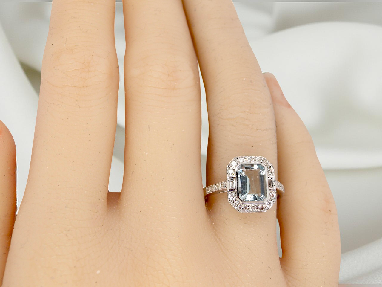 hand A very pretty cluster ring. Features a step cut aquamarine centre stone, 8x7mm (est 1.21 carats). Plain rim setting.