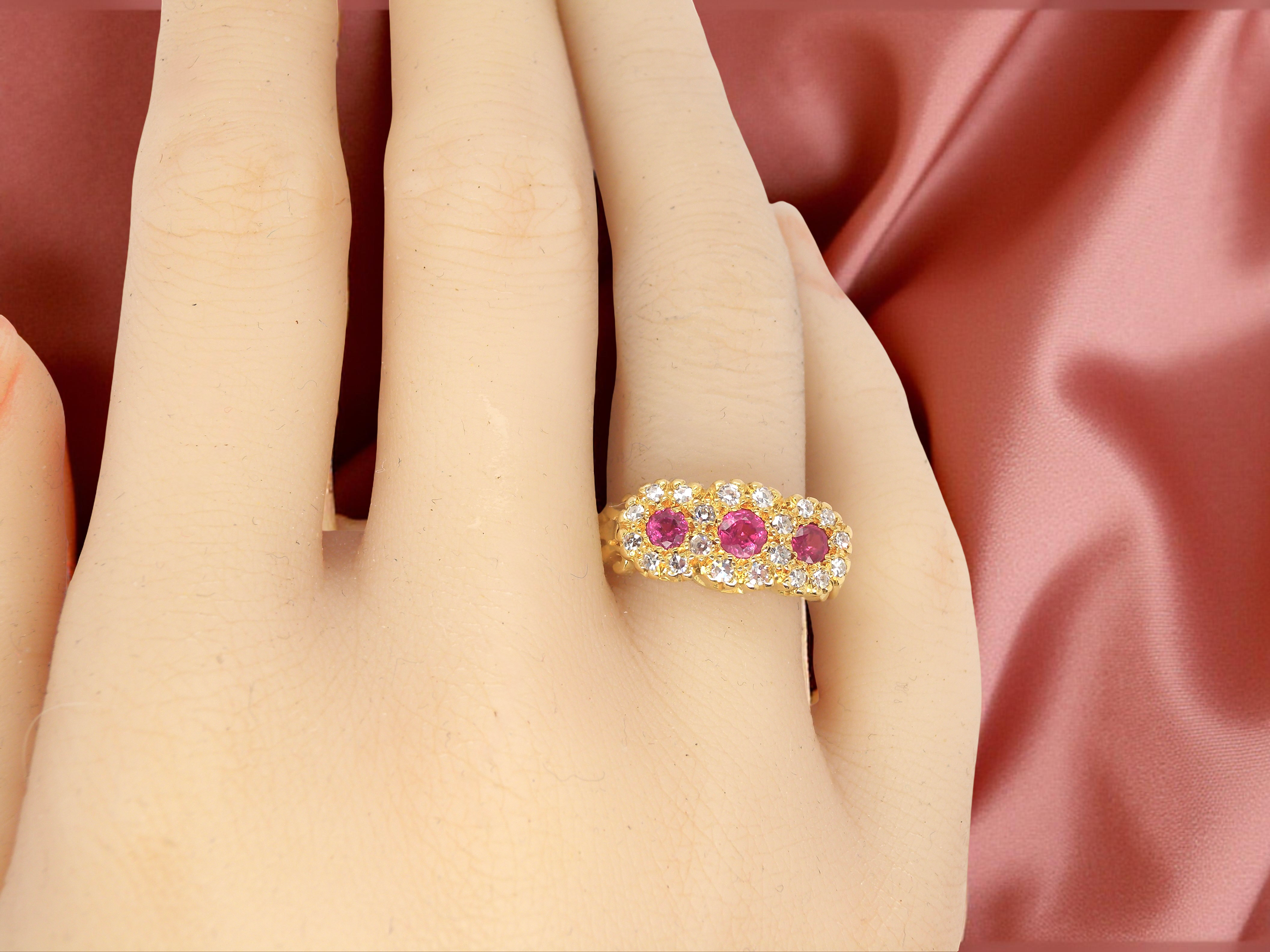 Gold ring with pink gemstones on a hand against a pink satin background