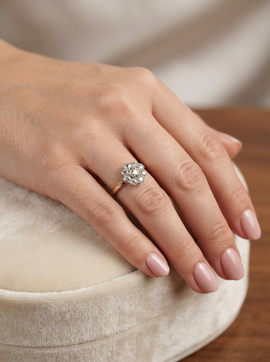 A close-up of a hand wearing a rose gold ring with a diamond cluster setting, resting on a cream velvet ring box.