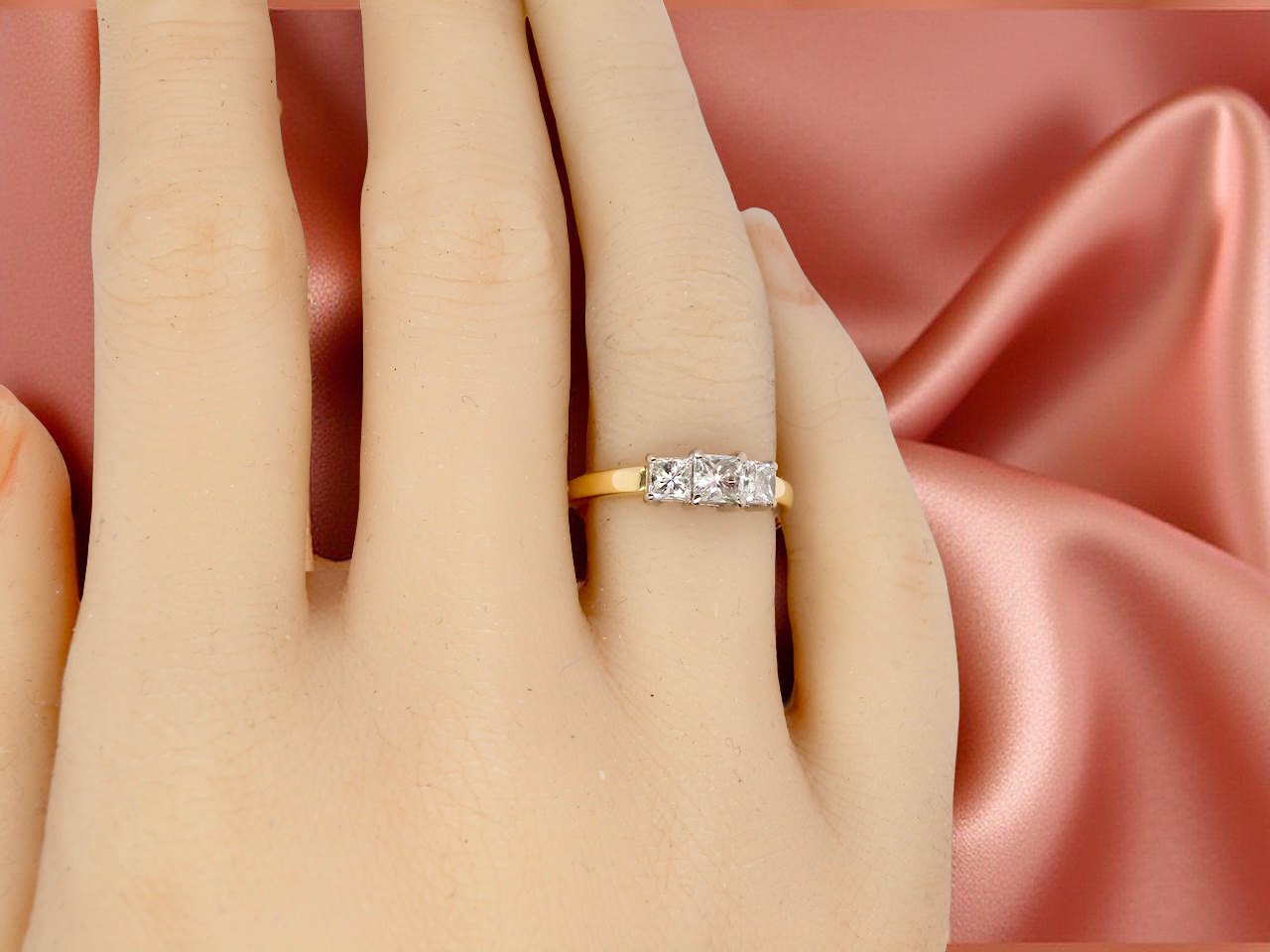 Gold ring with diamonds on a hand against a pink satin background