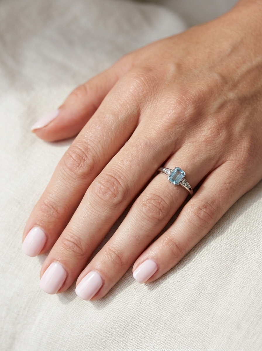 hand An 18 carat white gold ring, features a rectangular step cut aquamarine, measures 7x5mm (st one carat) sky blue, fine clarity. Rim setting.
