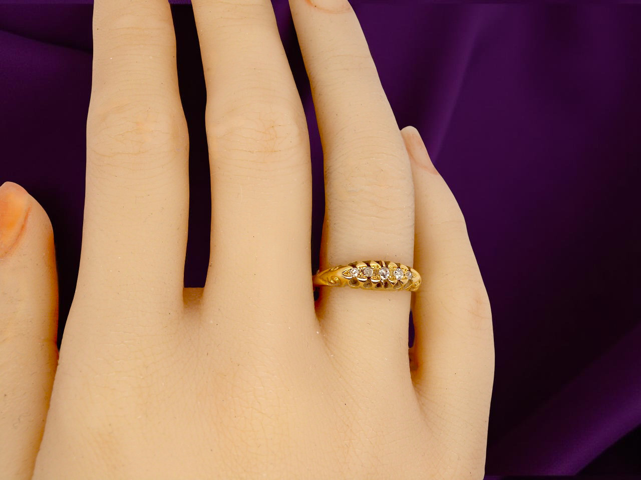 Gold ring with small diamonds on a hand against a purple background