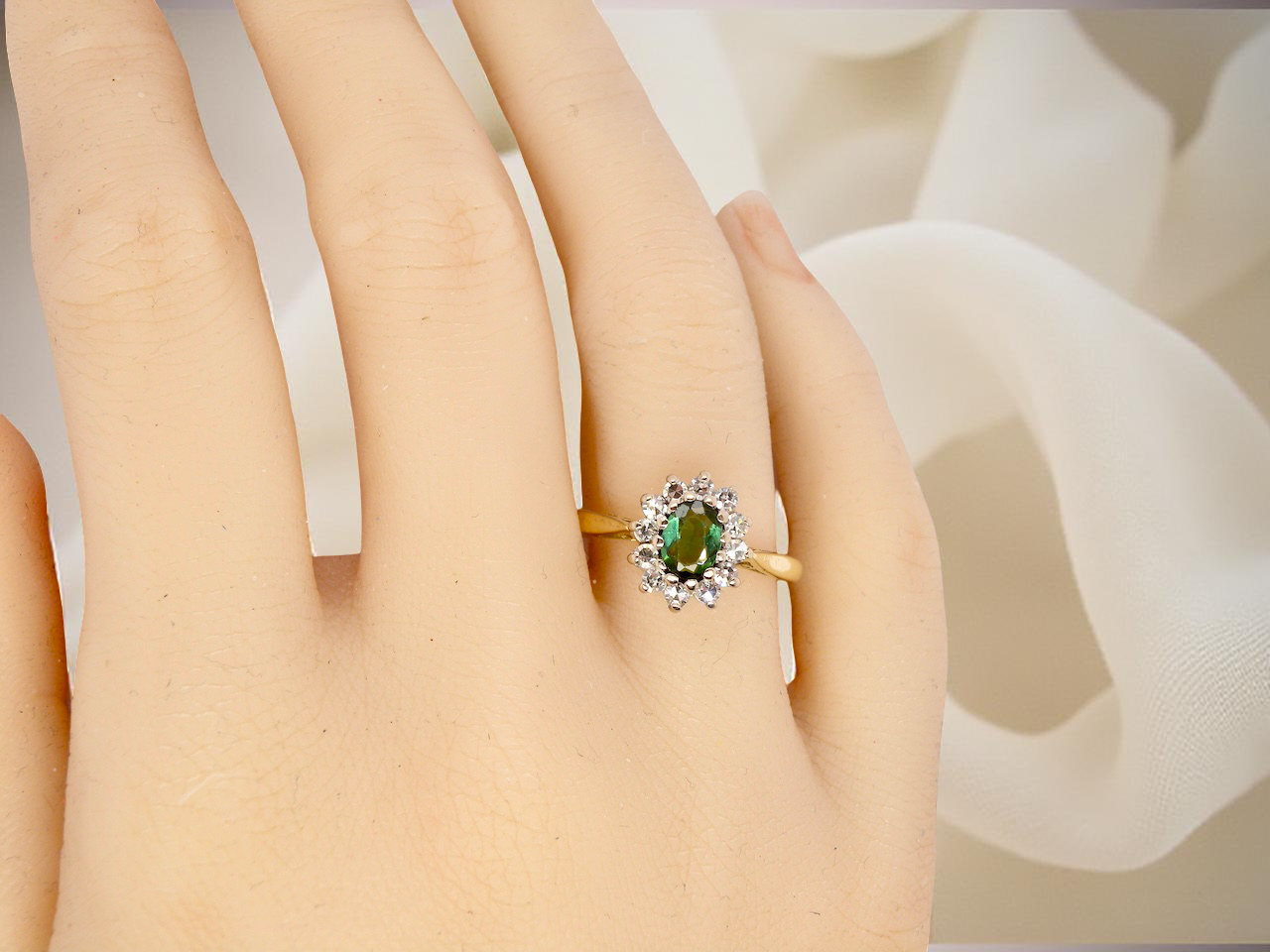 hand An elegant 18 carat gold cluster ring featuring a beautifully proportioned 6 × 4mm green tourmaline 