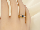 hand An elegant 18 carat gold three-stone ring featuring a rich, oval-cut dark blue sapphire at the centre, measuring 5 × 4mm, secured in a classic rim (bezel) setting.