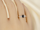 hand An elegant three-stone ring crafted in 18 carat white gold, featuring a striking rectangular dark blue sapphire at the centre, measuring 6 × 4 mm and weighing approximately 0.50 carats.