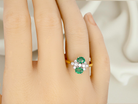 Ring with green gemstones on a person's finger against a neutral background