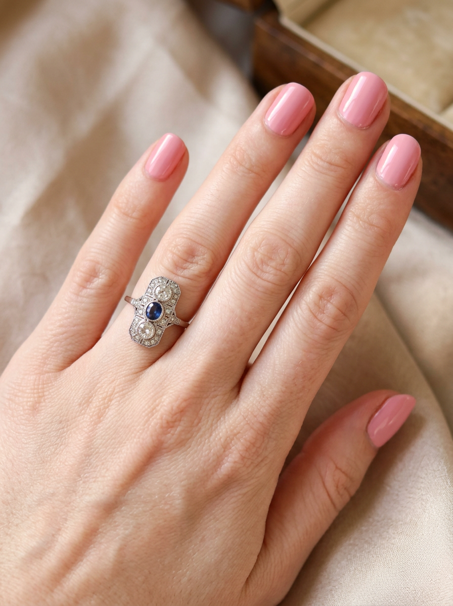 hand The plaque design has at its centre a mid to dark blue sapphire, 5x4mm (est 0.40 carats) mille grain set. Above and below to Old European Cut white diamonds. Each one estimated at 0.40 carats (4.8mm) Colour H-j, clarity Si.
