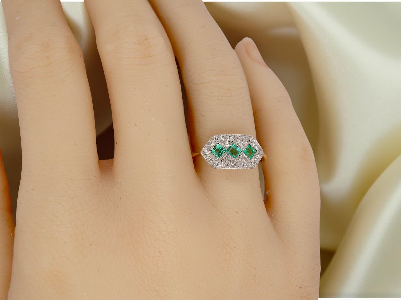 hand  fine Edwardian era cluster ring, beautifully handcrafted with a trio of vibrant emeralds surrounded by a halo of antique old-cut diamonds. 