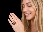 A close-up lifestyle shot of a smiling blonde woman wearing a geometric rose gold ring with clear stones, set against a solid black background.