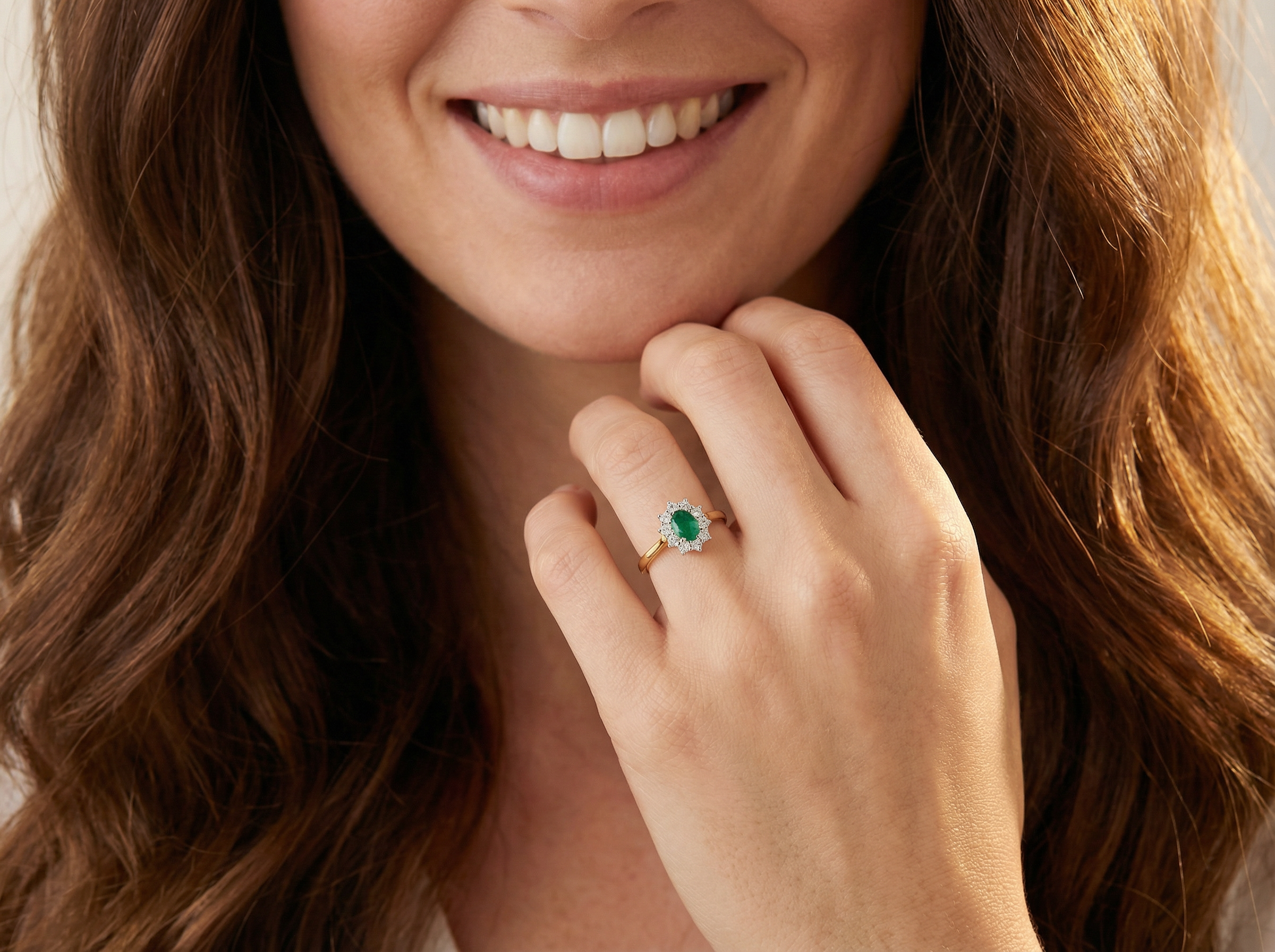 model A fine traditional emerald and diamond cluster ring, featuring a vibrant oval-cut emerald to the centre measuring approximately 7 × 5 mm 