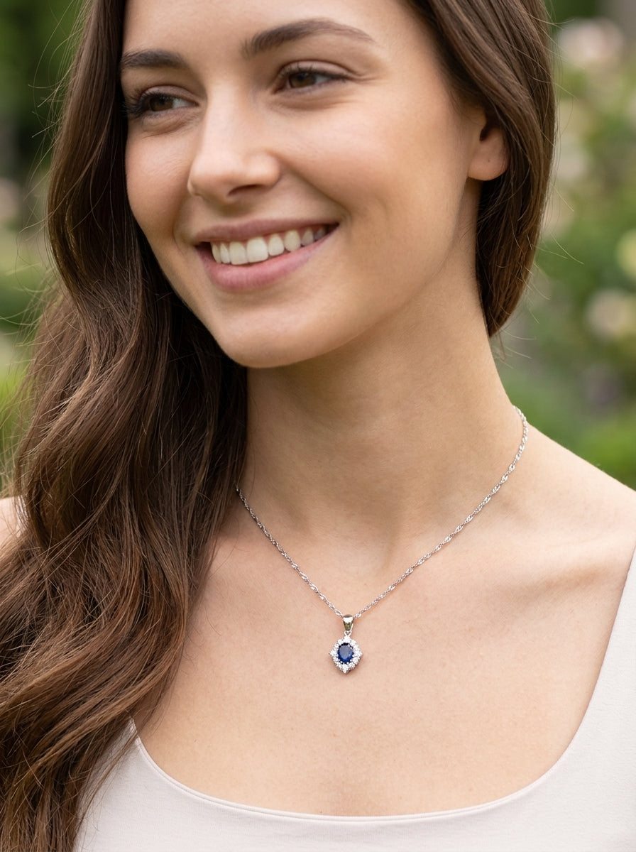 model A white gold pendant. The centre stone an inky black blue sapphire 7x5mm, claw set. Complimented by an outer halo of twelve brilliant cut white diamonds.