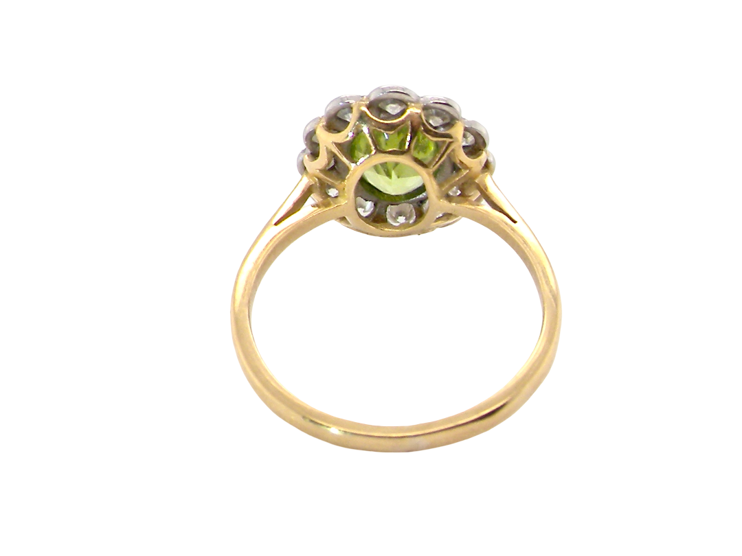 A yellow gold ring featuring a central light green peridot gemstone surrounded by small clear stones in a decorative setting, shown on a plain white background.