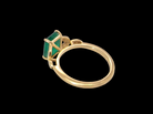 A yellow gold ring featuring a rectangular green emerald-cut gemstone in a prong setting, accented with small clear stones along the band, shown against a solid black background.