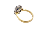 A vintage-style ring with a yellow gold band and a silver-toned floral cluster setting featuring dark blue and clear stones, shown on a plain white background.