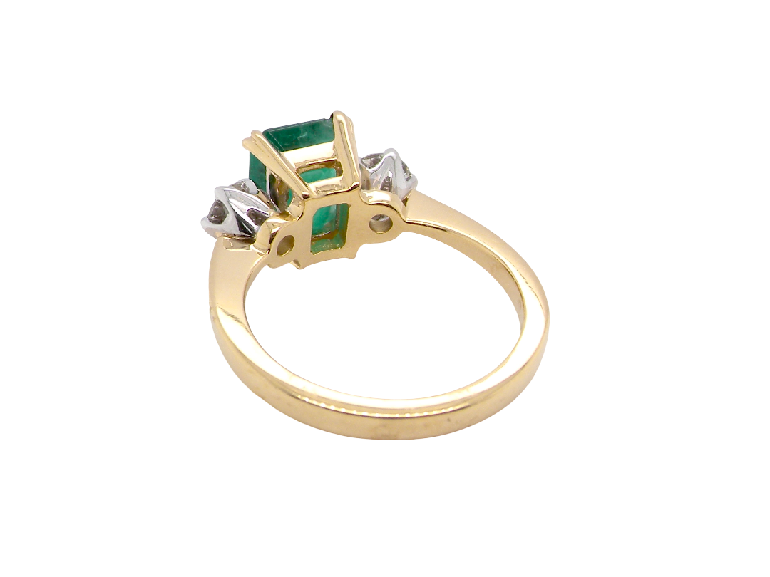 rear An exceptional three-stone ring featuring a vibrant step-cut emerald to the centre, measuring 8.6 x 7.0mm and weighing approximately 2.10 carats. The emerald displays a beautiful grass-green colour and is secured in a classic four-claw setting.