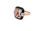 A rose gold ring featuring a rectangular emerald-cut pink gemstone in a bezel setting with a black enamel border, accented by two small round clear stones on either side, shown on a plain white background.