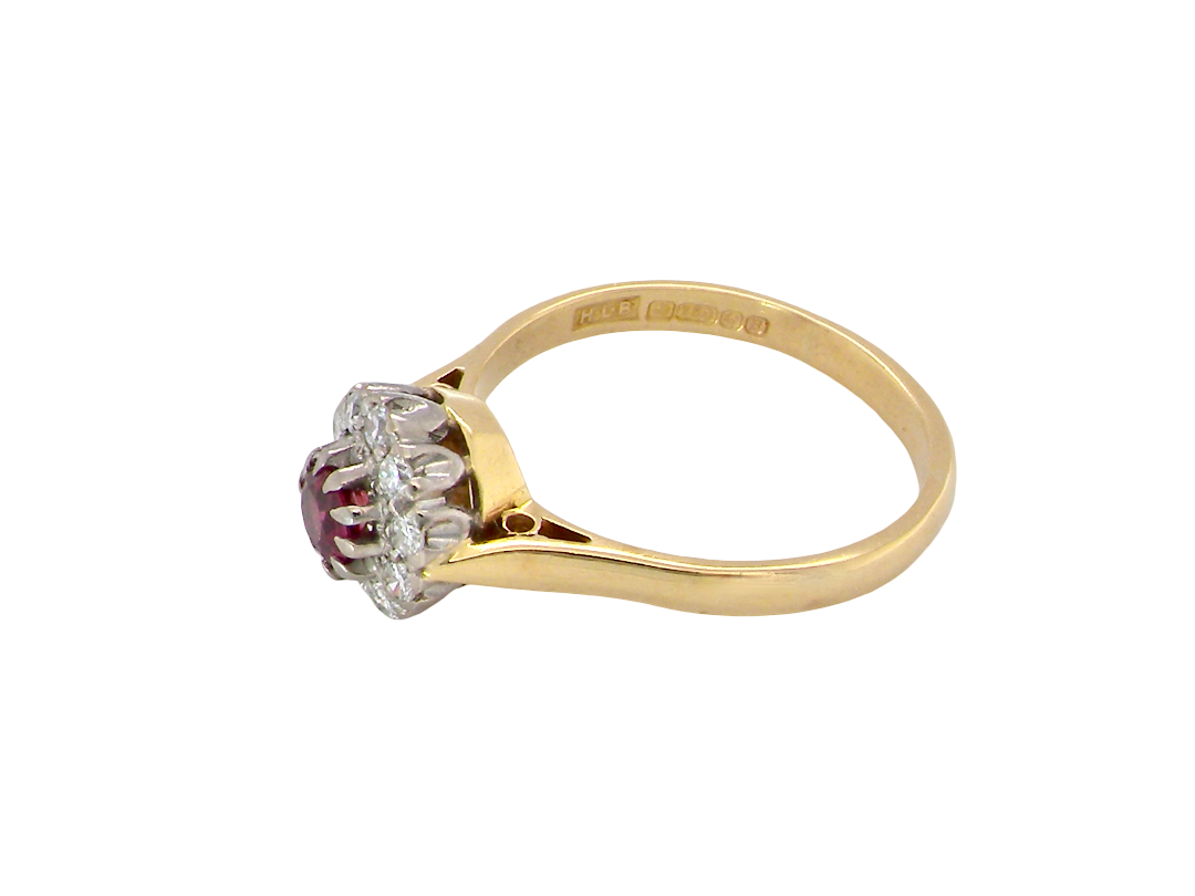 A vintage yellow gold ring with a central cluster of clear stones and a round red ruby gemstone, shown on a plain white background.