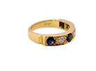 A vintage yellow gold ring featuring round blue sapphires and a central clear diamond, shown on a plain white background. The inside of the band is stamped with '18CT'.