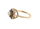 A vintage-style gold ring featuring a cluster of white opal gemstones and small dark blue stones, set on a polished yellow gold band against a plain white background.