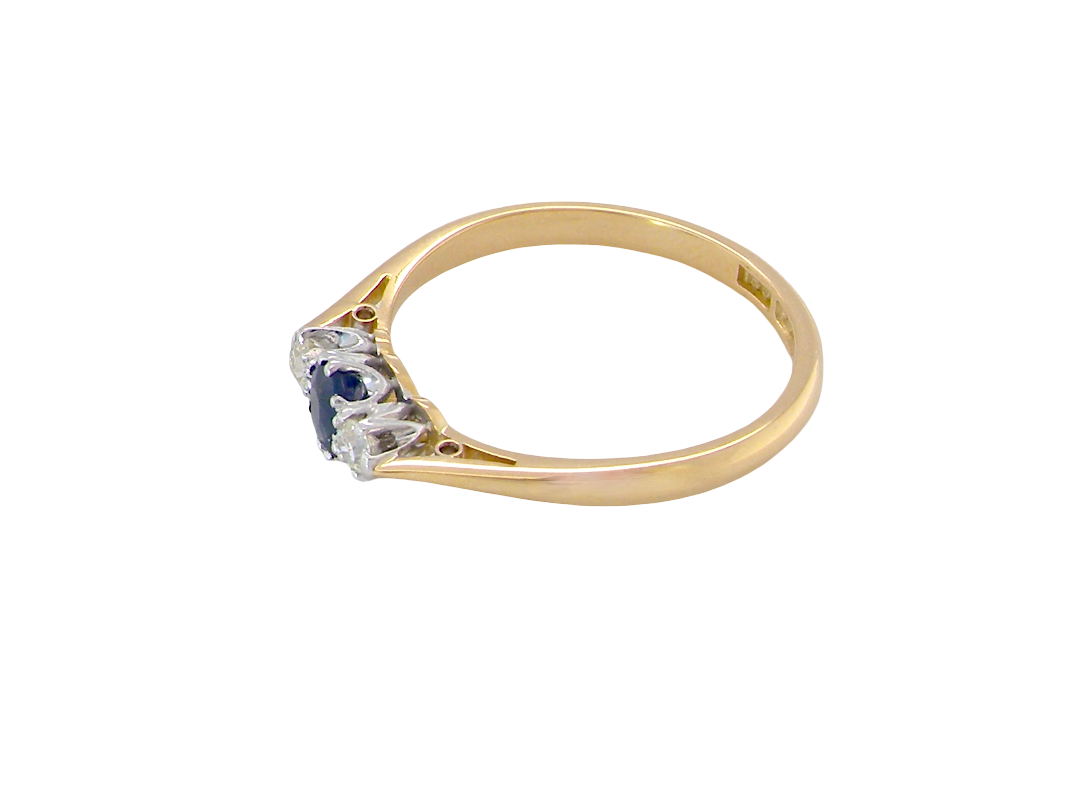 side The classic trilogy ring, this features to the centre a round mid to dark blue sapphire and each side a brilliant cut white diamond