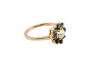 A yellow gold ring featuring a flower-shaped setting with dark blue gemstones and a central white pearl, shown on a plain white background.