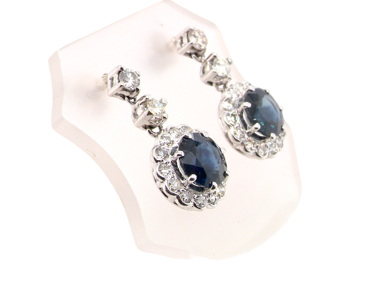 side view An exquisite pair of drop earrings crafted in 18 carat white gold, each set with a striking inky blue-black sapphire measuring 7.5mm in diameter.