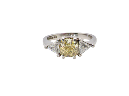 striking and elegant trilogy ring crafted in 18-carat white gold, set with a vibrant fancy yellow cushion-cut diamond