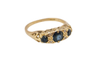 A yellow gold ring featuring three oval dark blue sapphires and small clear accent stones, set against a plain white background.