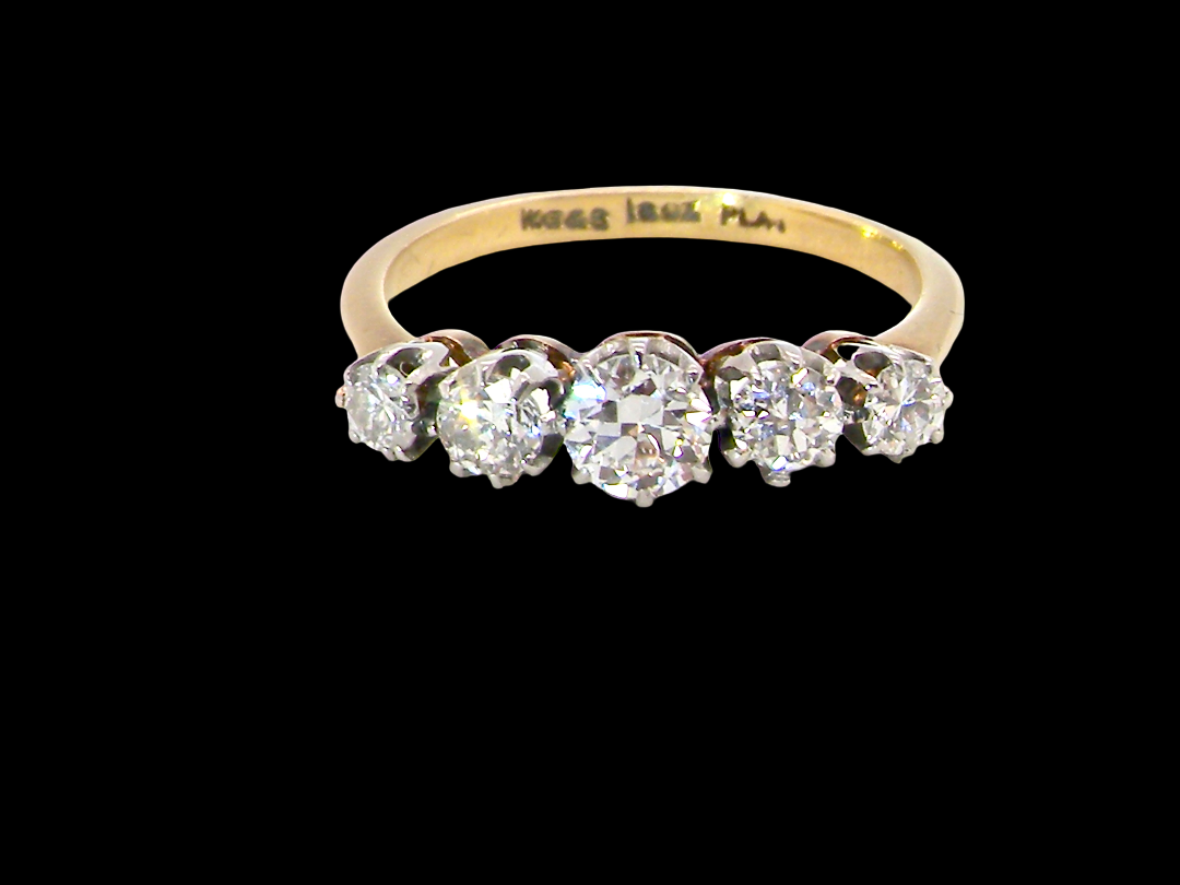 A five-stone diamond ring with a yellow gold band, set against a solid black background. The inner band is engraved with 'MOSES 18.