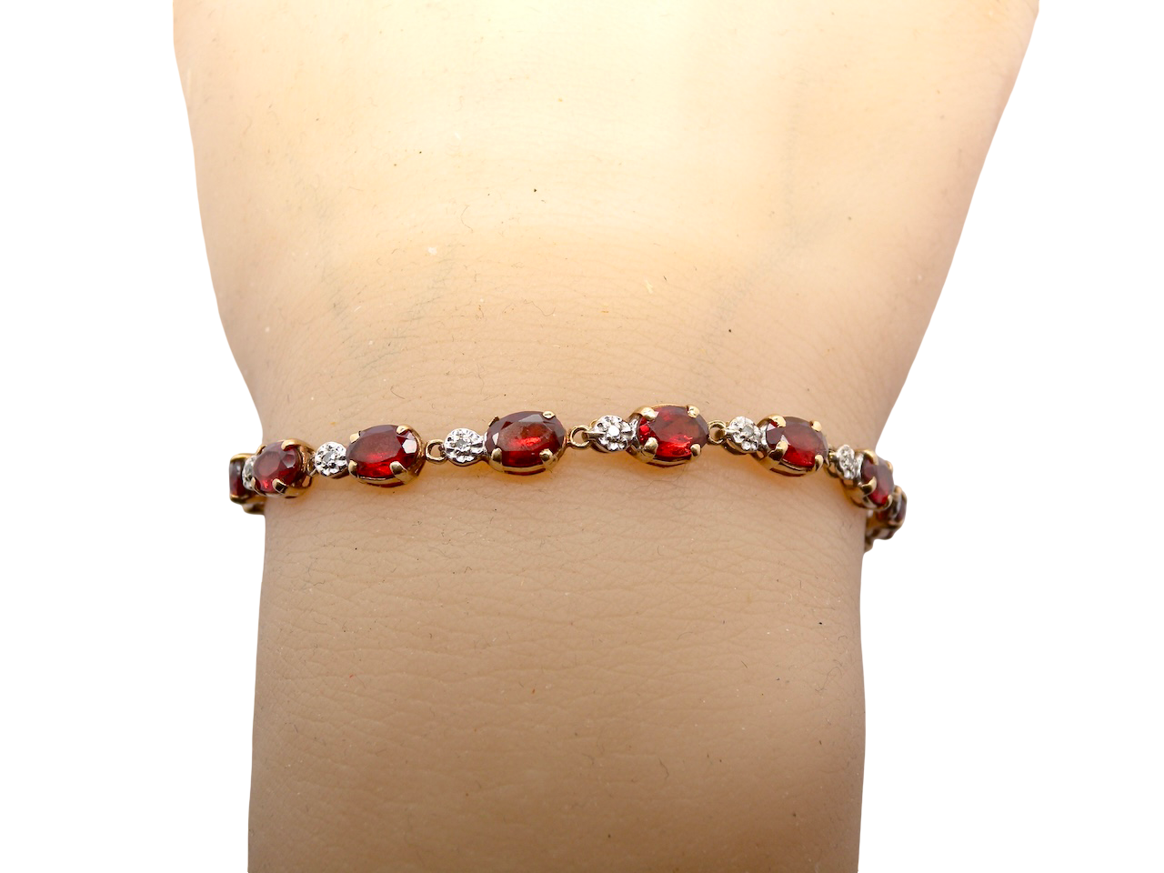 wrist An elegant 9 carat gold bracelet set with sixteen rich red oval-cut garnets, each measuring approximately 6 x 4mm. Between each garnet sits a delicate illusion-set diamond in white gold, creating the appearance of larger stones while adding subtle sparkle. The total diamond weight is estimated at 0.15 carats.