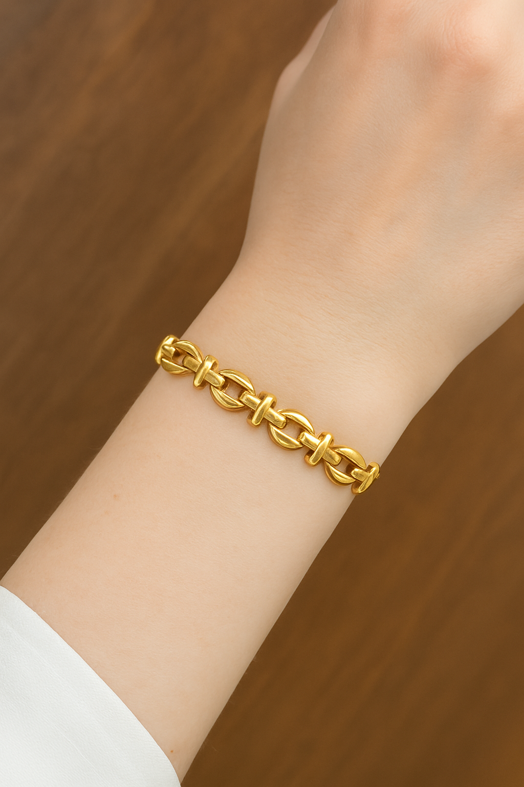 Gold chain bracelet on a wrist against a wooden background